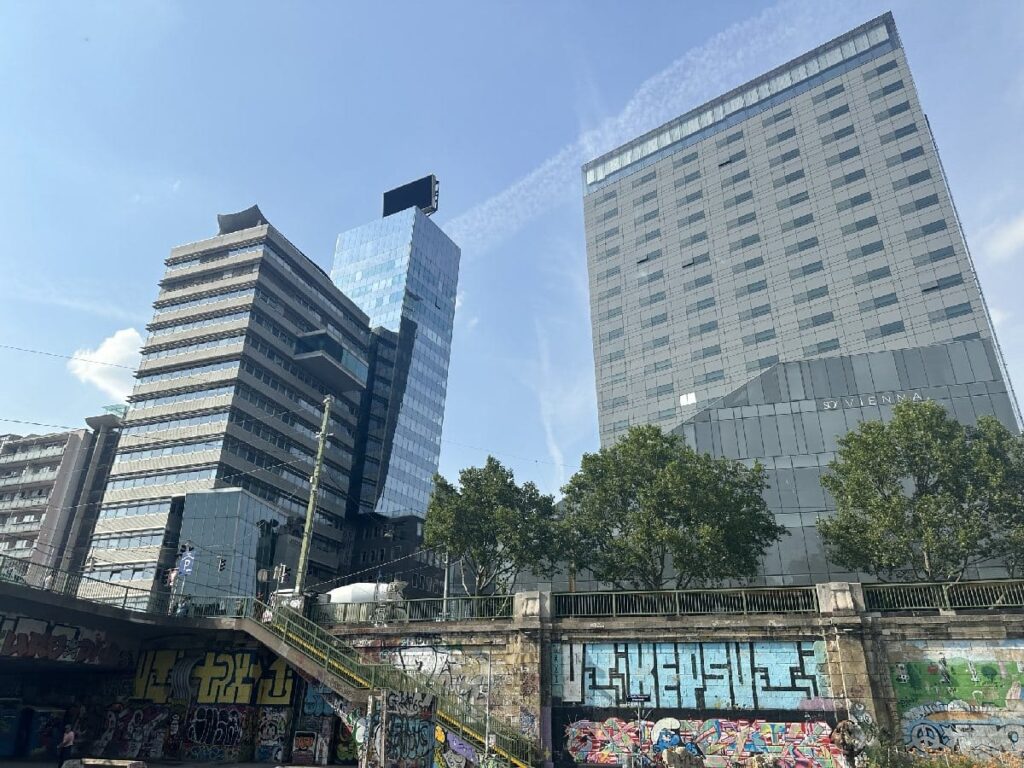 Three modern buildings with glass facades and a graffiti wall in the foreground.