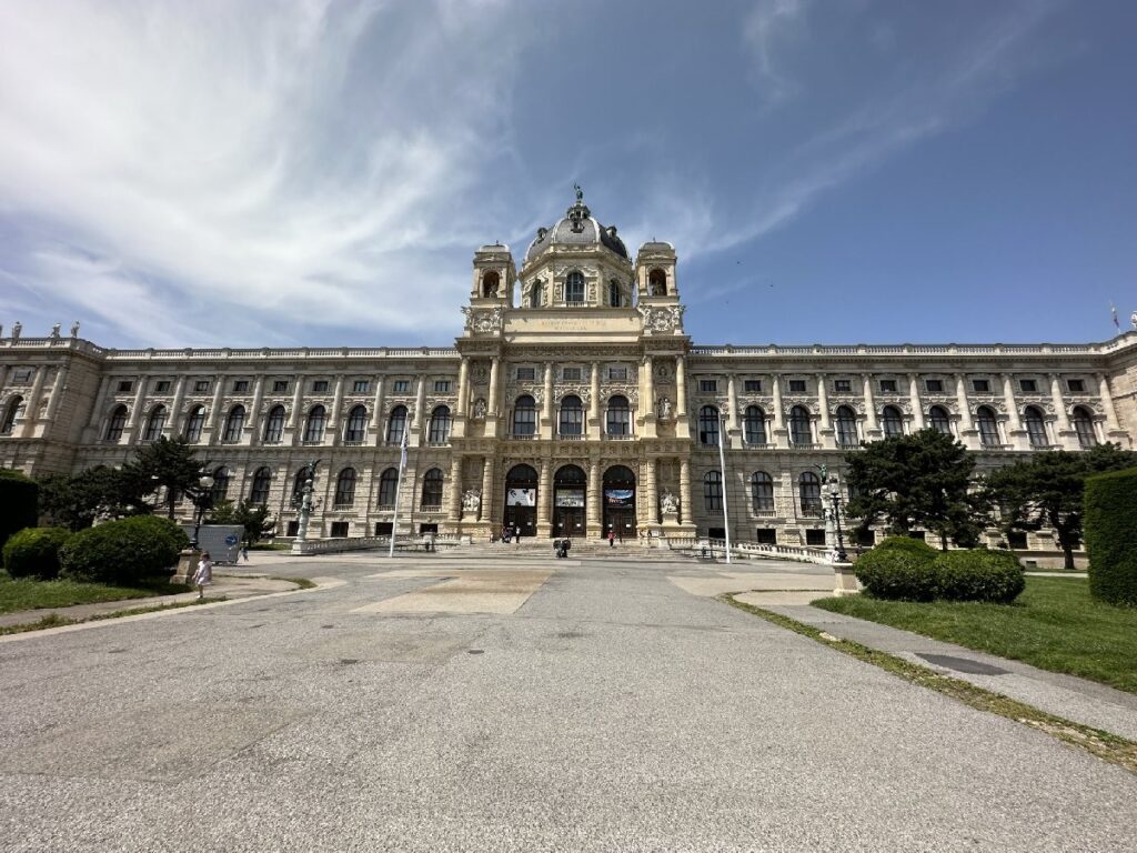 Historic building with impressive architecture in Vienna, featuring a central façade and large entrances, surrounded by well-maintained green spaces.