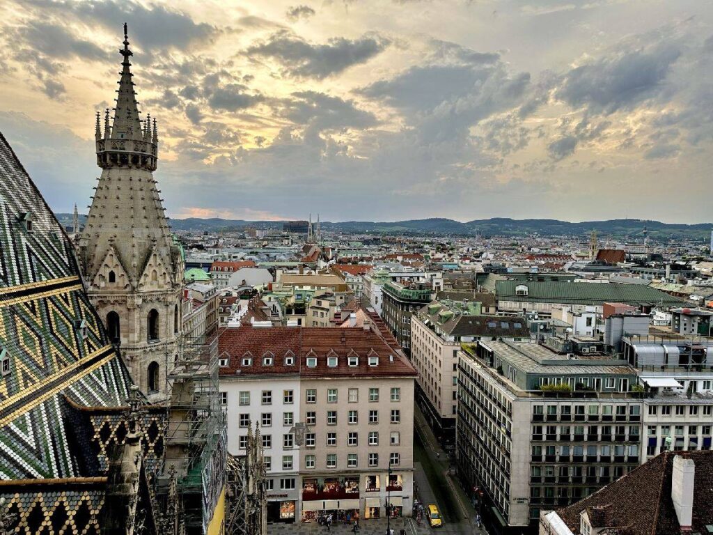 View of the city of Vienna with historic buildings and a striking tower in the foreground, under a cloudy sky.