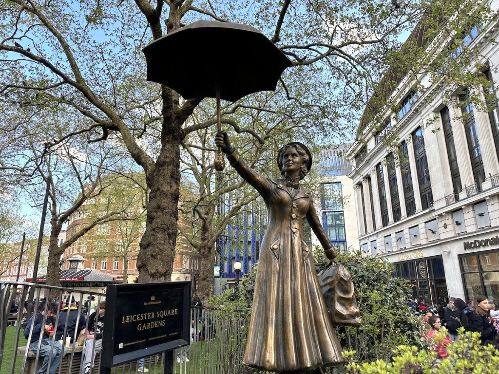 Bronze statue of a woman holding an umbrella in Leicester Square Gardens.