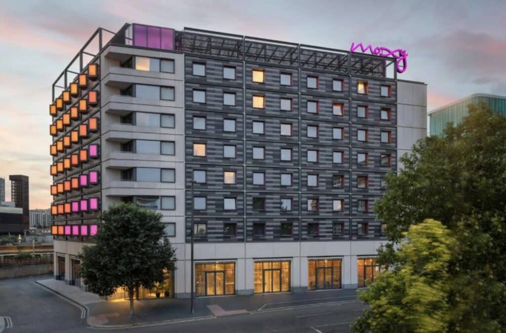 Moxy Hotel in London Stratford mit moderner Architektur und bunten Lichtern an der Fassade, mehrere Fenster sichtbar.