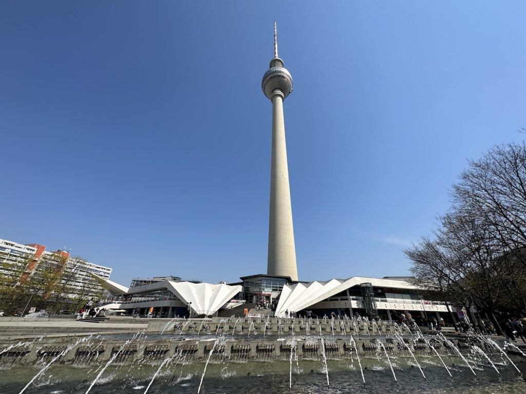 The Berlin TV Tower rises above Alexanderplatz, where visitors gather around the fountains.