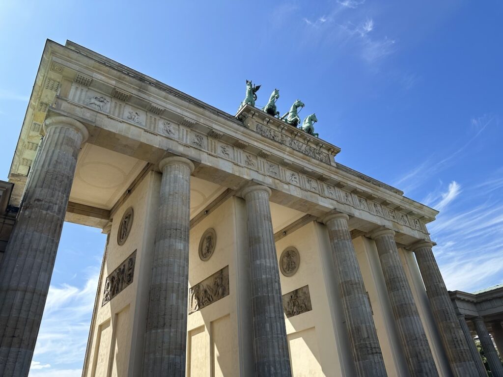 Seen from below, the Brandenburg Gate’s stone columns and sculpted quadriga rise against a clear Berlin sky.
