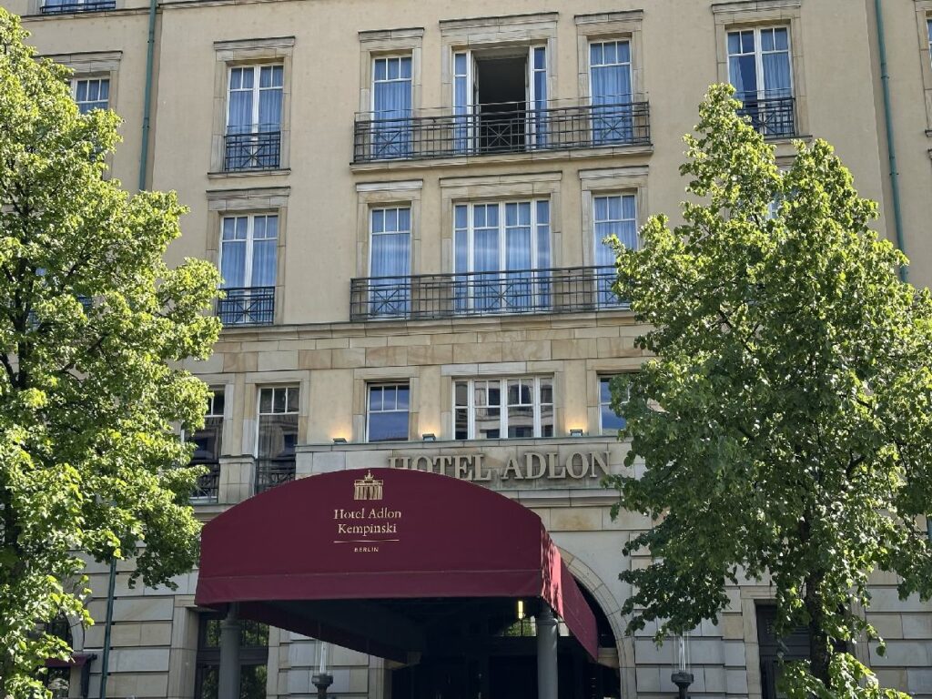 Entrance of Hotel Adlon Kempinski in Berlin-Mitte, with its burgundy canopy, stone facade and green trees.