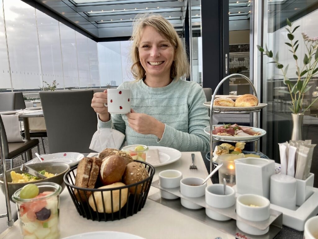 Woman enjoying breakfast with coffee, fresh bread, fruit and a tiered serving stand at Käfer Restaurant in the Reichstag building in Berlin.