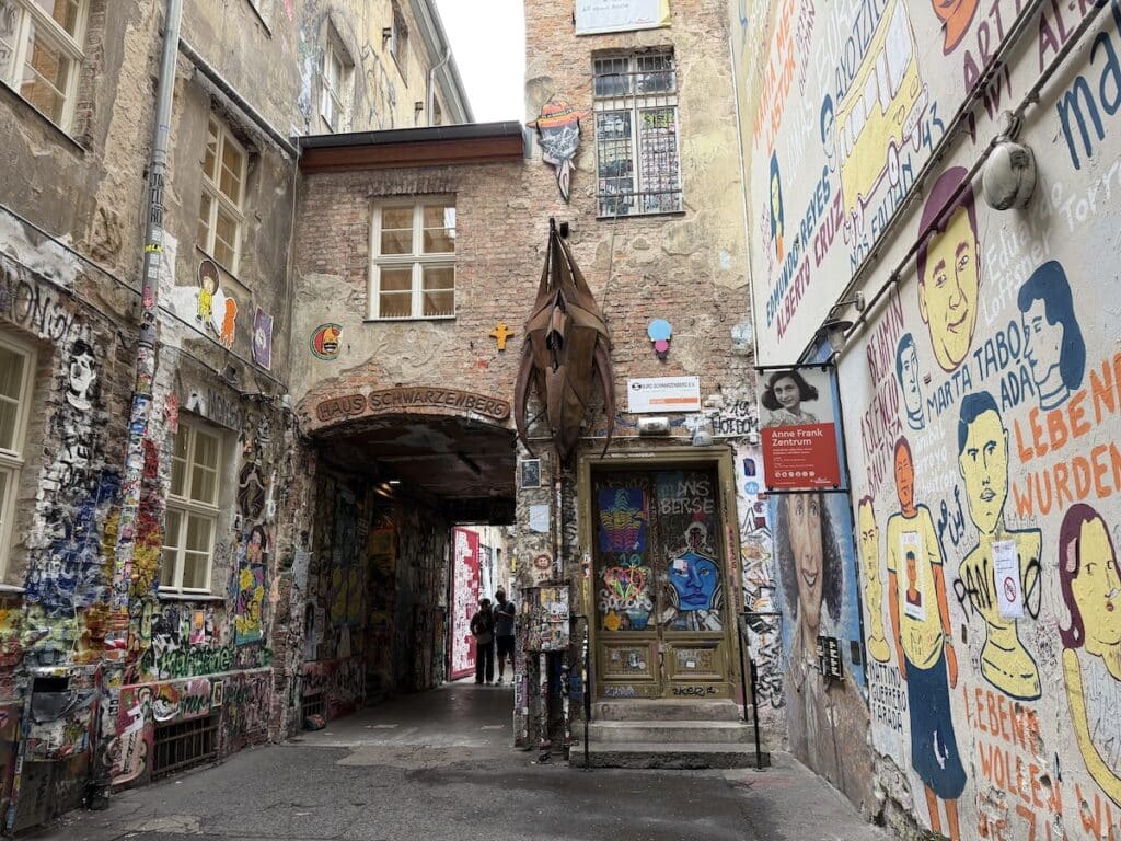 Graffiti-covered Haus Schwarzenberg passage in Berlin, with colorful murals, posters, a courtyard entrance, and an Anne Frank Zentrum sign.