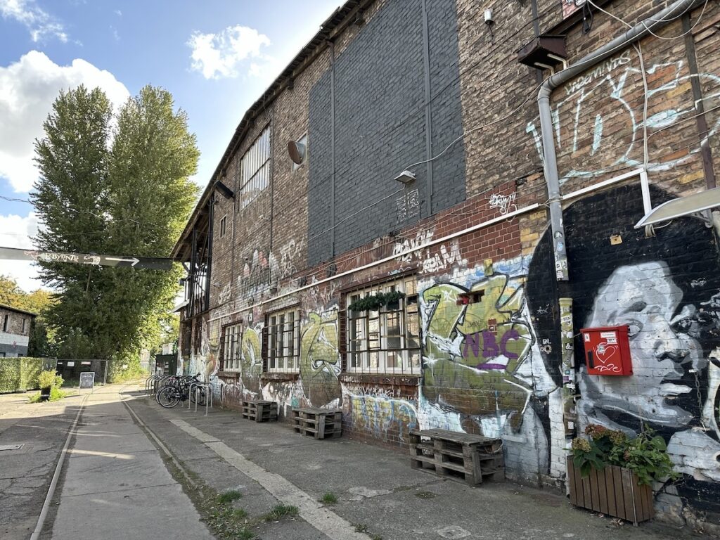 Graffiti covers a brick building along a quiet Berlin lane, where bicycles stand by the windows and a sign points toward Labyrinth.