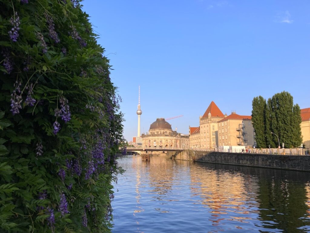 Purple wisteria frames Berlin’s Museum Island, with the Berlin TV Tower and historic domed buildings reflected in the Spree.